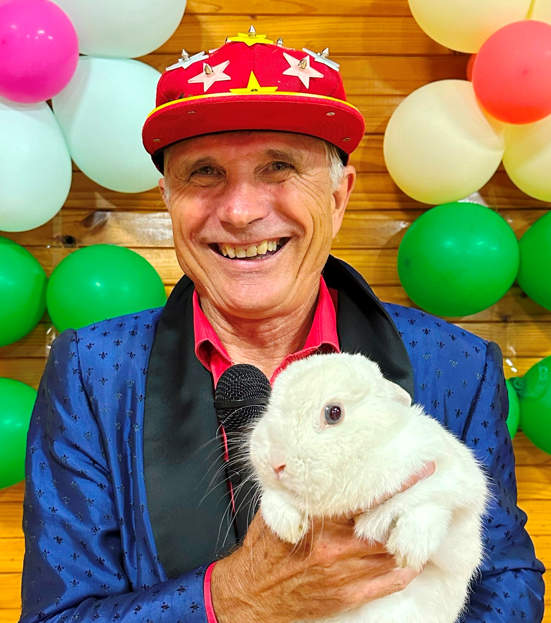 Balloonatic Bruce holding Ally Kazam, the real live magic rabbit, in front of a colorful balloon wall